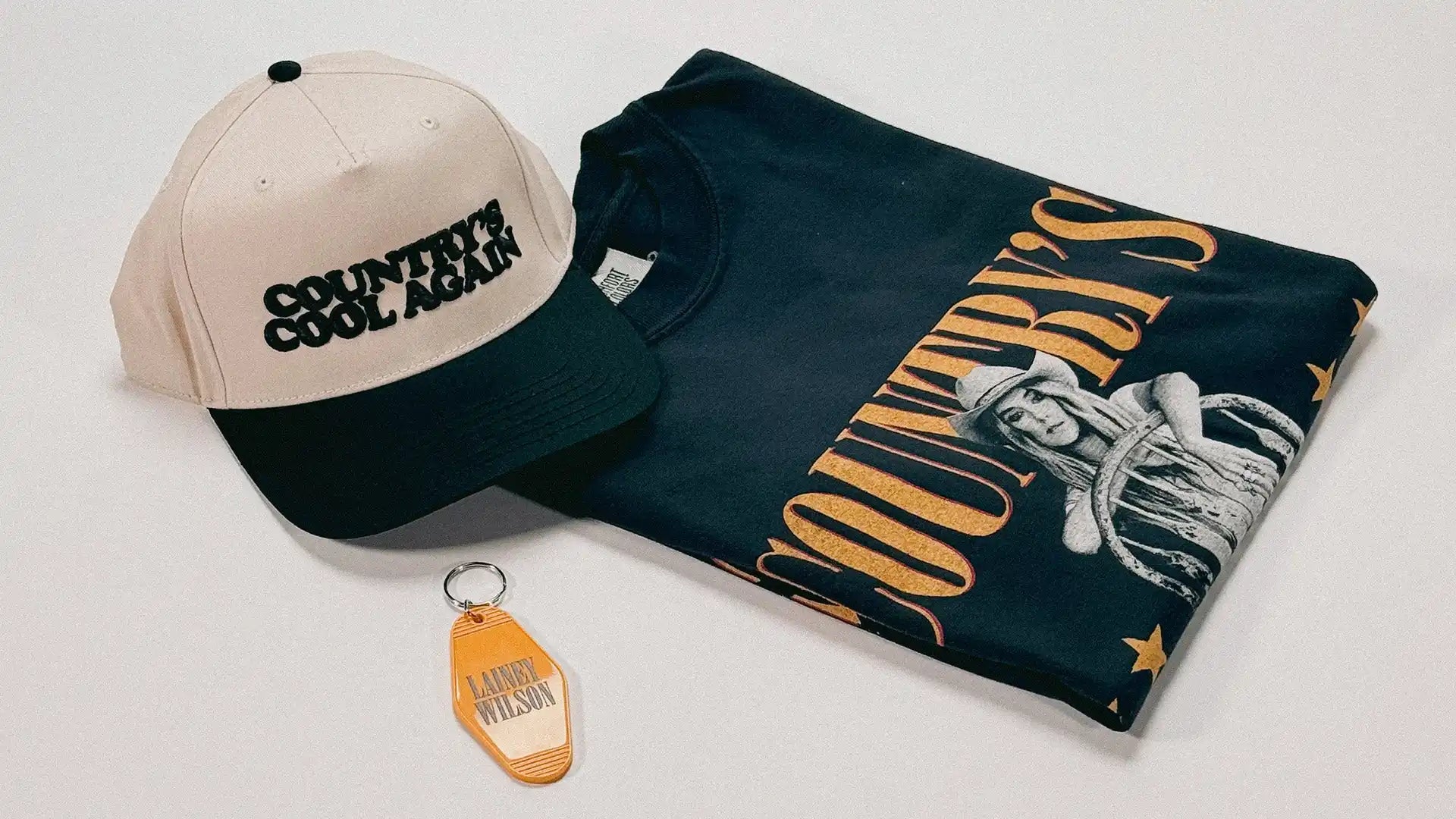 A black and beige baseball cap, a black t-shirt with a graphic design, and an orange keychain.
