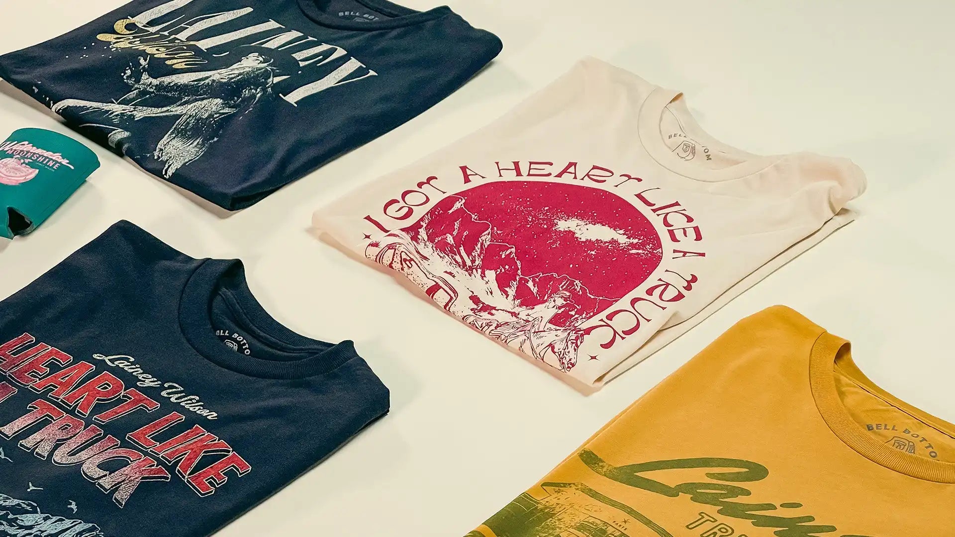 Four folded graphic t-shirts of various colors.