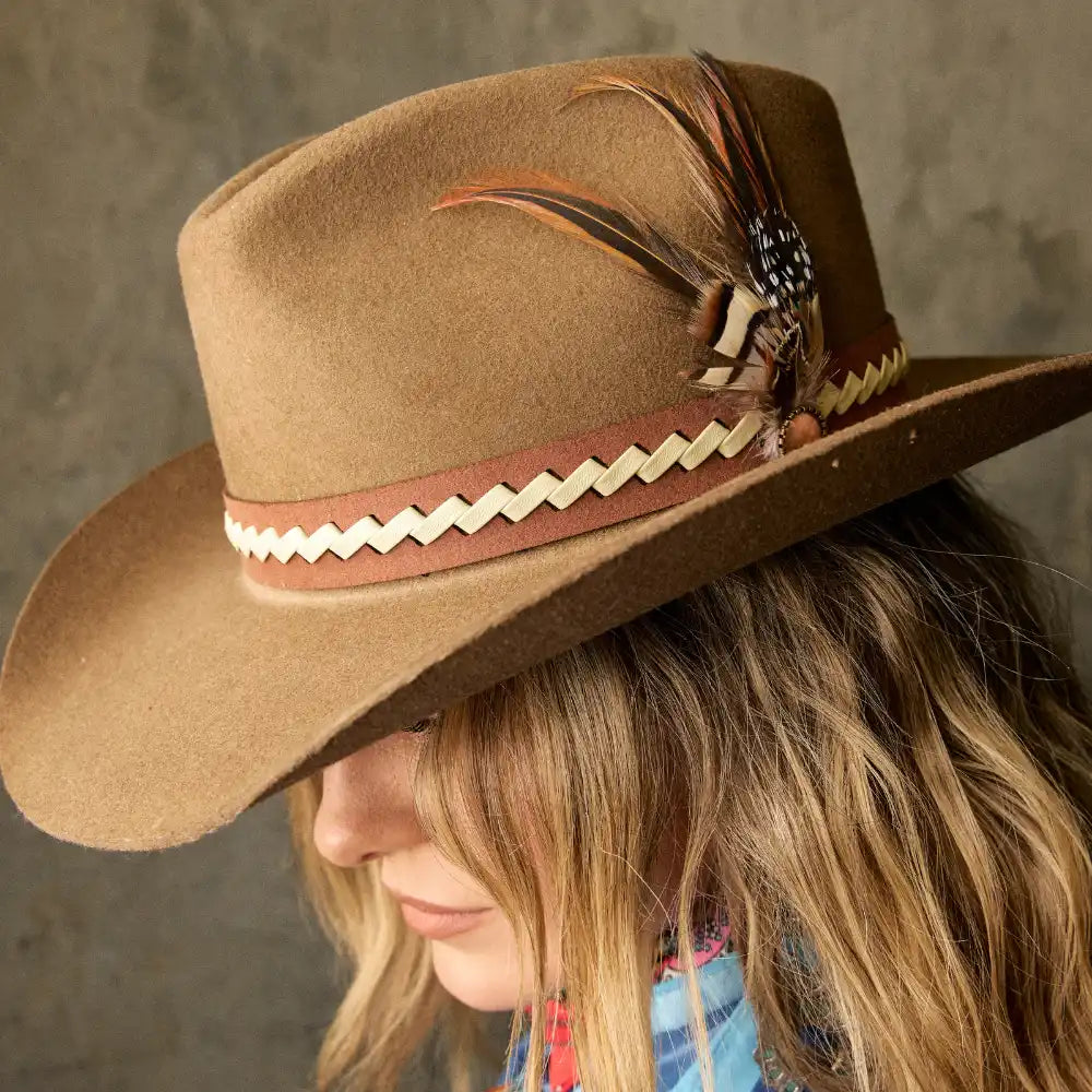 A tan felt cowboy hat with a decorative band and feathers.
