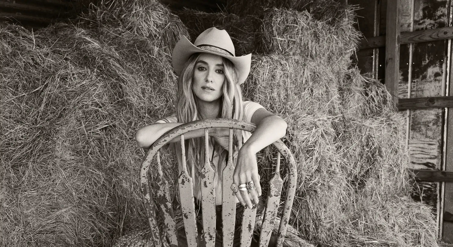 A woman in a cowboy hat leaning on a rustic wooden chair.