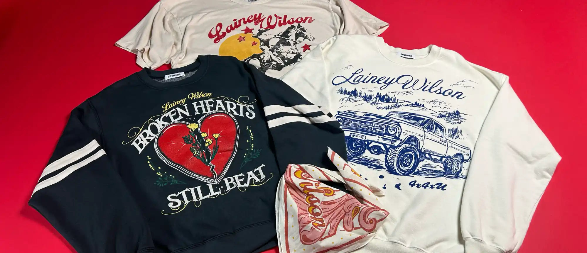 A collection of Lainey Wilson branded apparel, including a t-shirt, two sweatshirts, and a bandana.